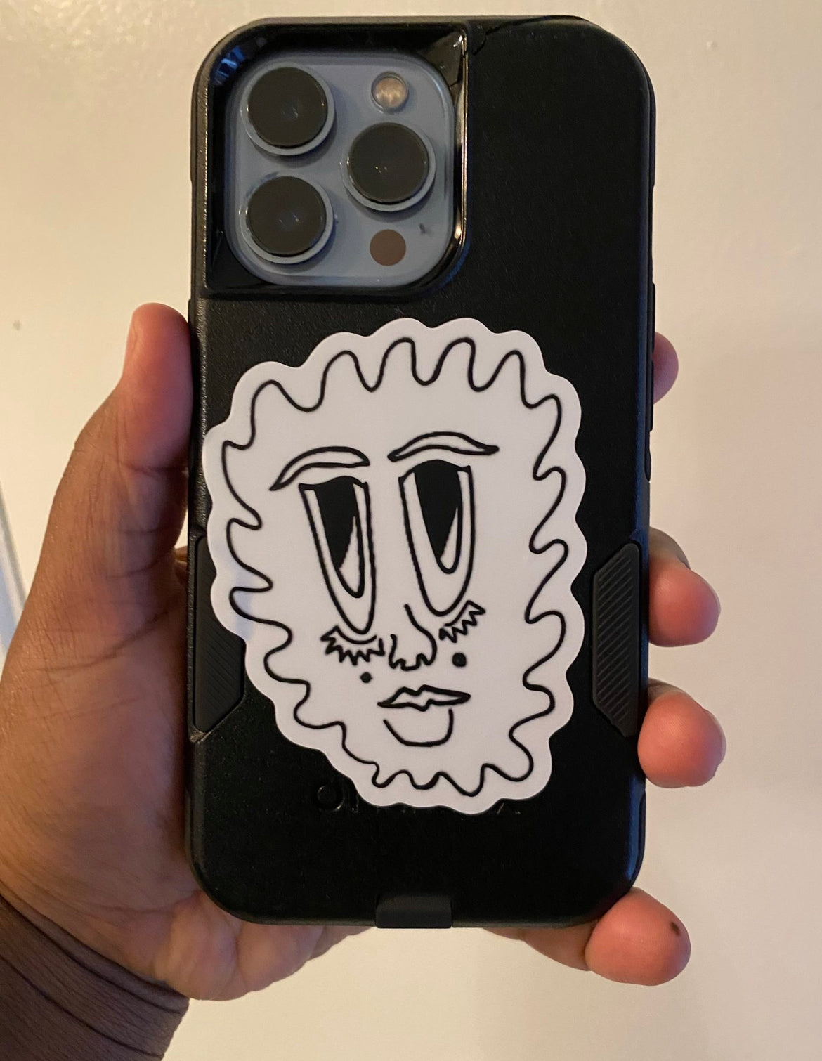 "floating face" sticker being shown on the back of the artist's phone